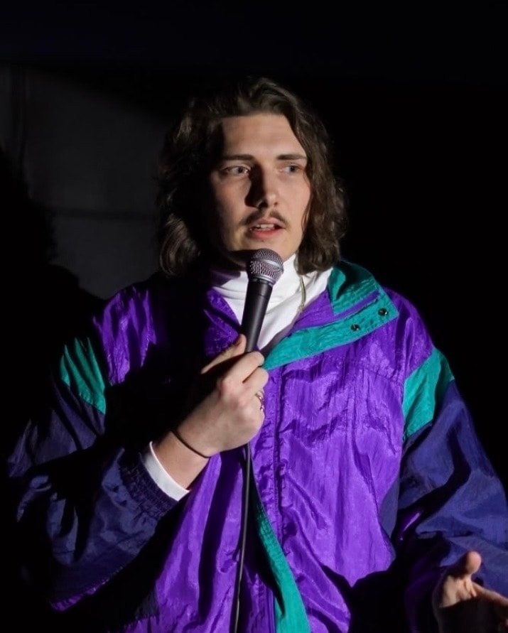 Comedian in purple windbreaker jacket performing with microphone